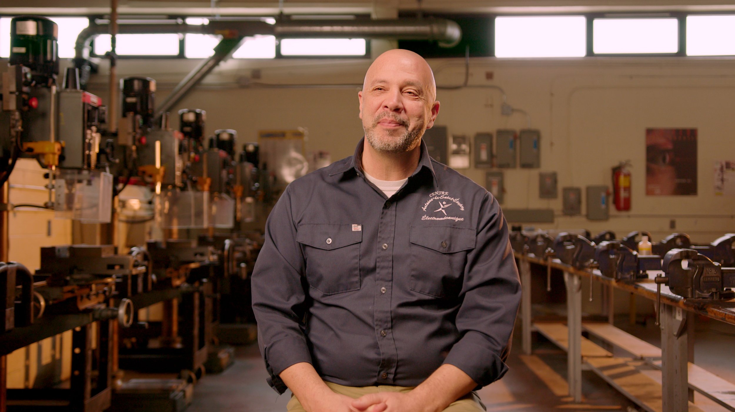 Un homme souriant portant une chemise avec logo dans un atelier de menuiserie.